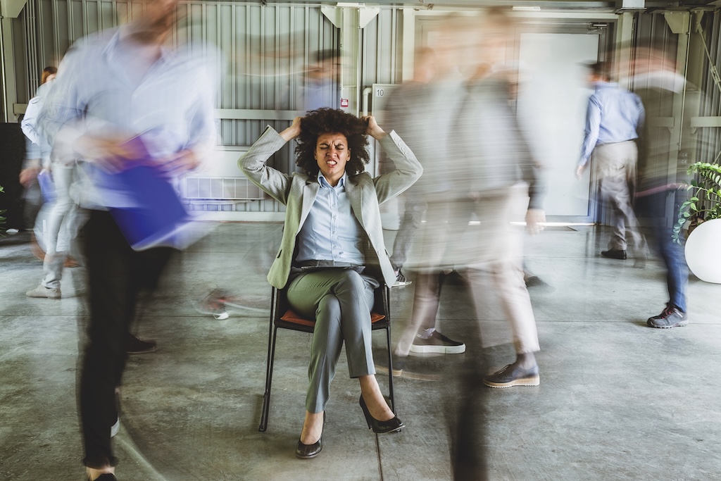 Black woman manager pulling her hair surrounded by colleagues rushing about.