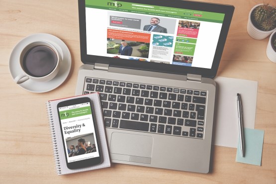 Phot of office desk with a laptop and phone displaying MiP website