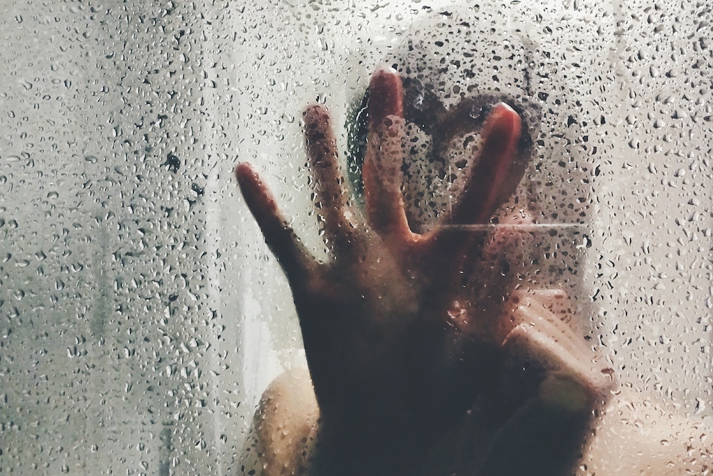 Woman's hand drawing heart on wet window