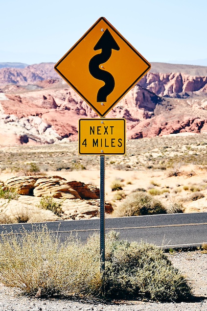 Sign in desert indicating dangerous bends for 4 miles