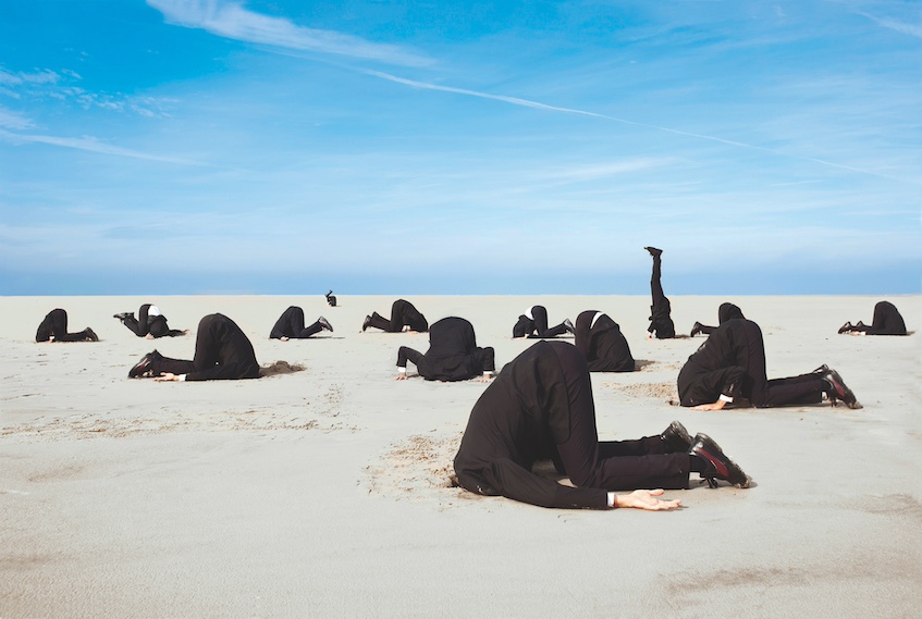 Group of men in suits with heads buried in the sand