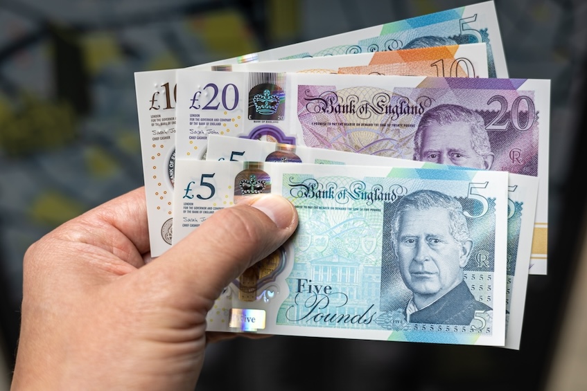 Man's hand clutching a selection of new banknotes featuring King Charles